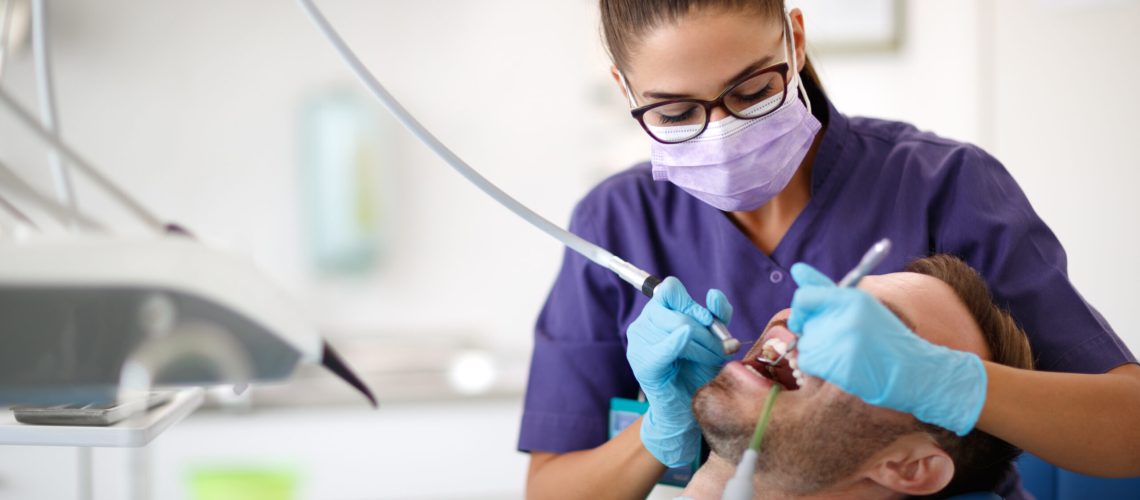 Young female dentist drilling tooth to patient in dental clinic