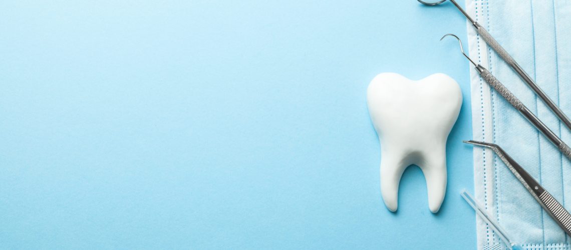 Tooth and dental instruments on blue background. Dental treatment. Dentist tools mirror, hook, tweezers, syringe. Copy space for text