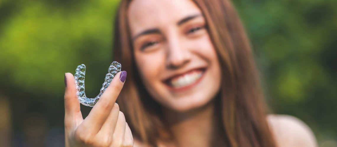 Beautiful smiling Turkish woman is holding an invisalign bracer with vibrant colors